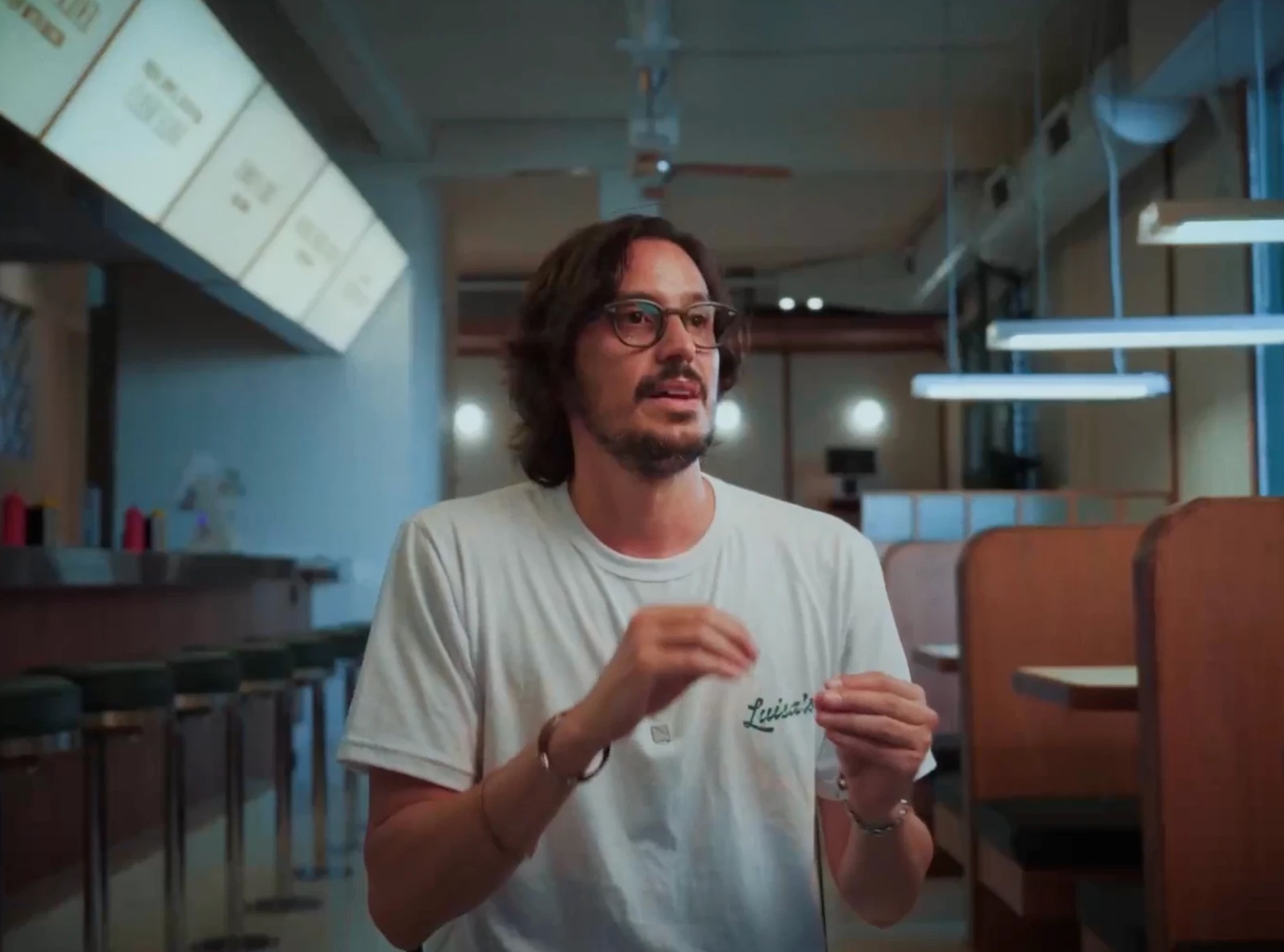 Entrevistado con remera de Luisa's hablando a cámara, con luz fría de fondo