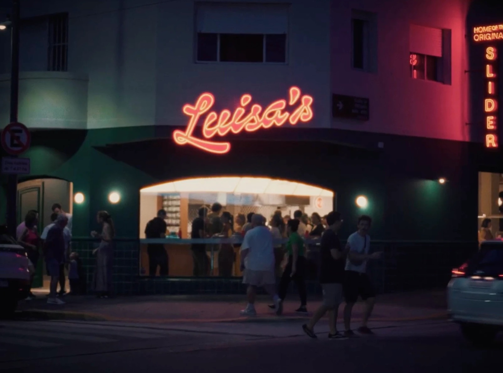Fachada de Luisa's de noche, con el cartel de neón y gente en la vereda