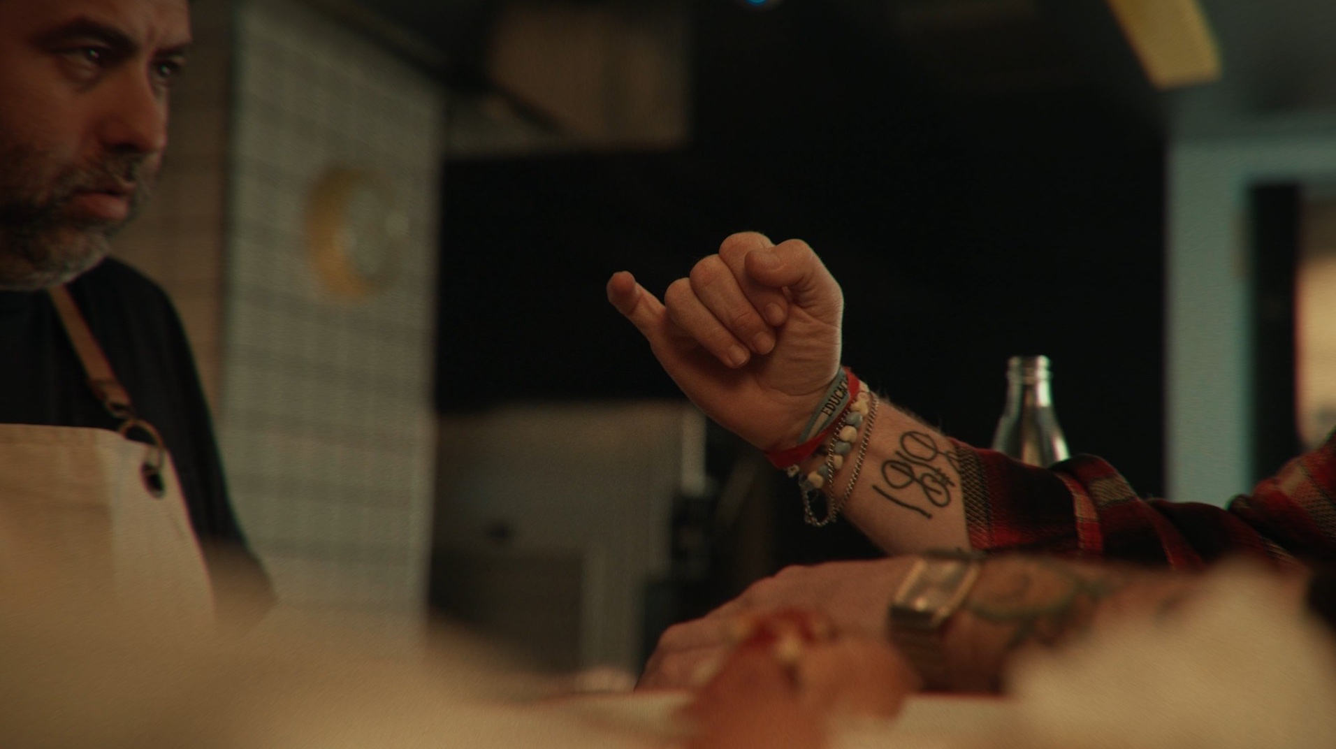 Detalle de la mano tatuada de un cliente, con el cocinero desenfocado