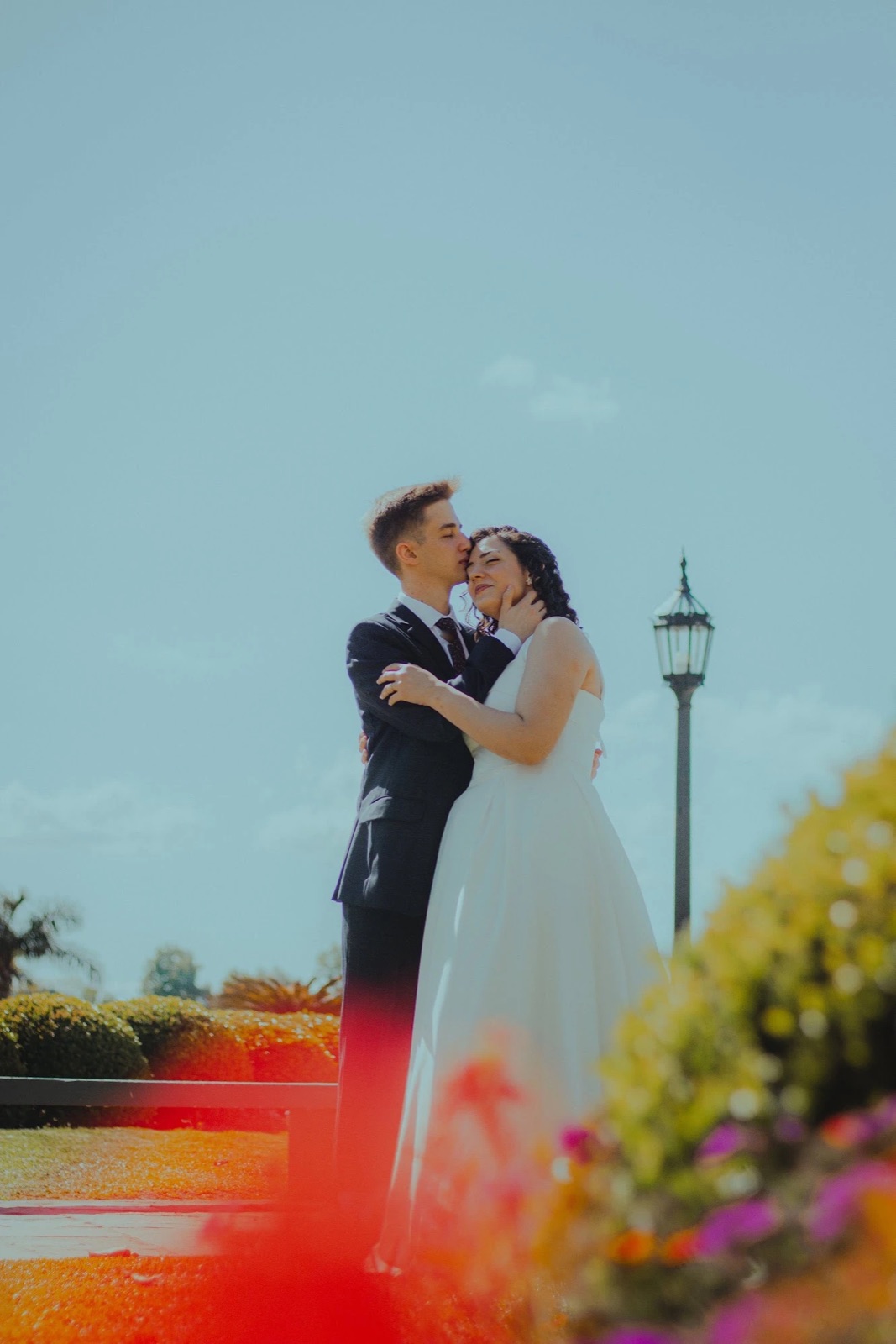 Agus kisses Ani's forehead by a lamppost, among flowers