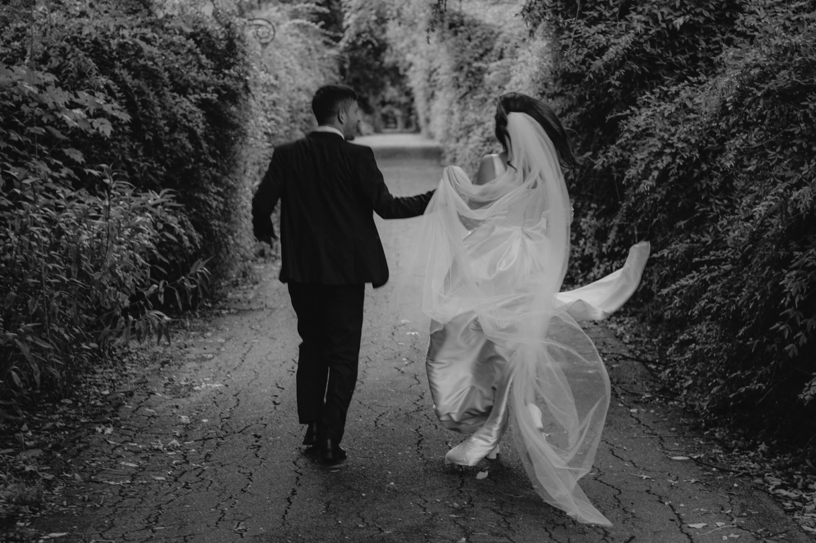 Paco and Mica run hand in hand along a hedge-lined path