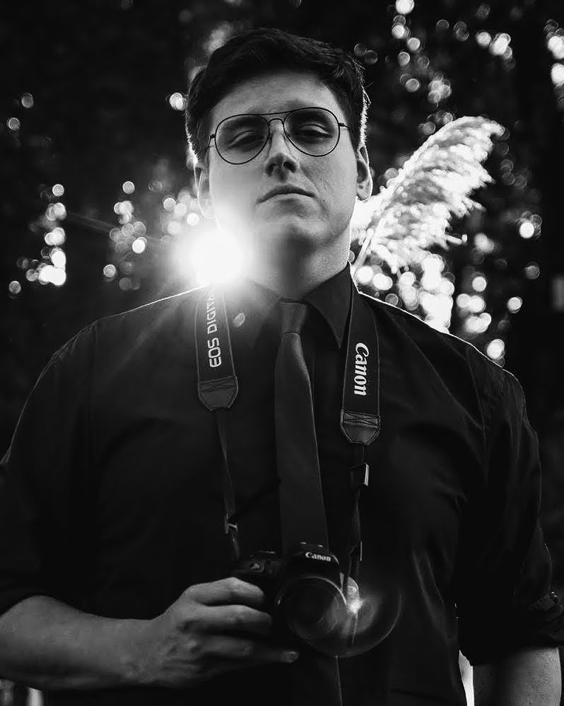 Retrato de Kevin Bahamondez con su cámara colgada, a contraluz, en blanco y negro