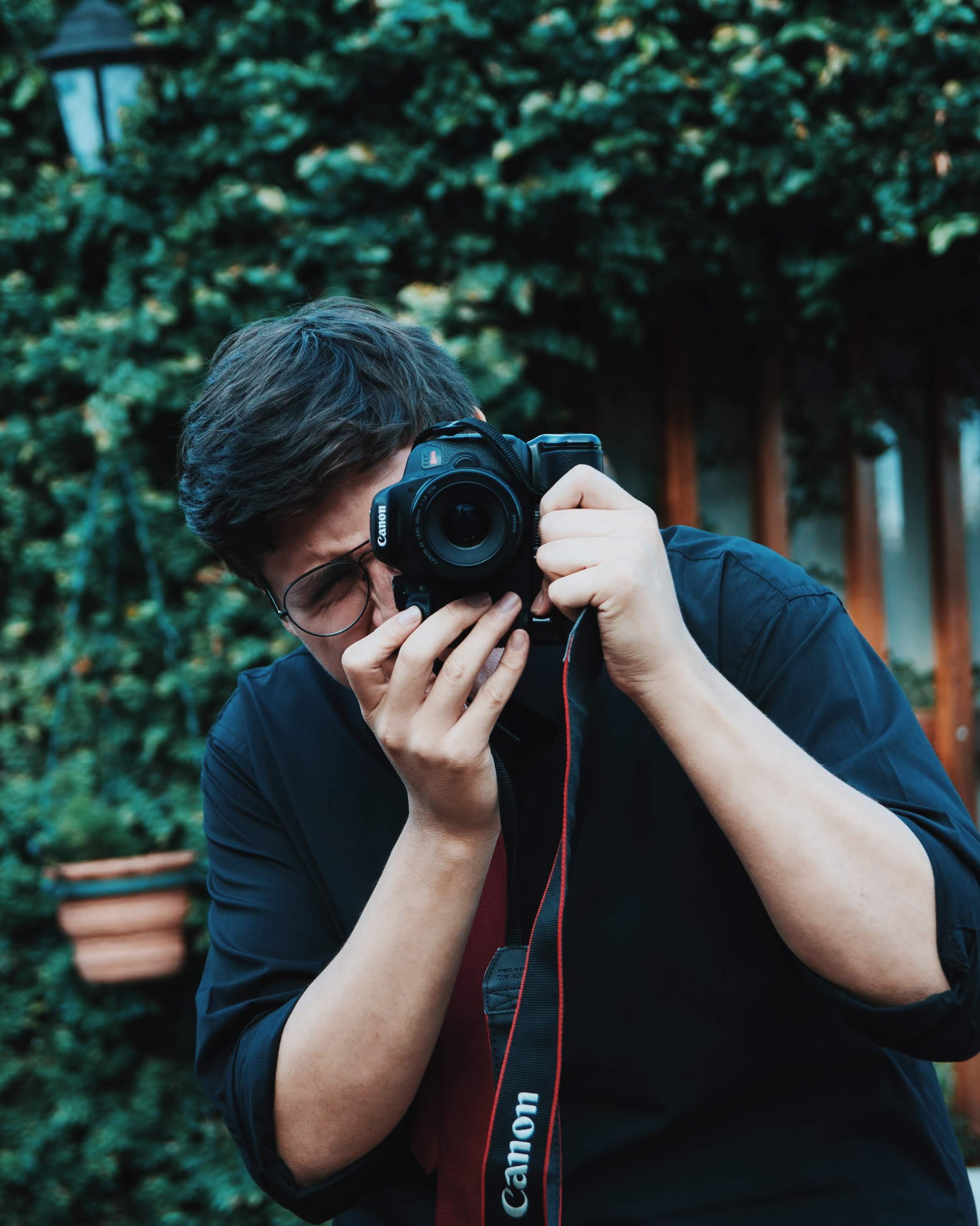 Kevin Bahamondez points his camera at you in front of an ivy-covered wall
